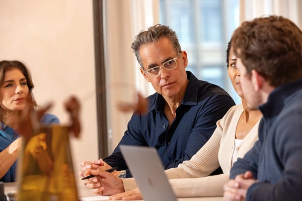 Three colleagues discussing work around a table with a laptop.